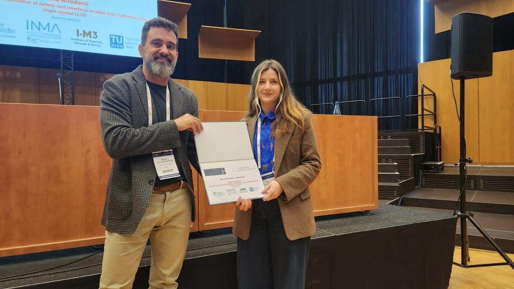 Two people holding a certificate on a stage at an event.